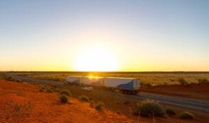 A large truck, an unsung hero of Australian logistics, drives on a deserted highway during a sunset.