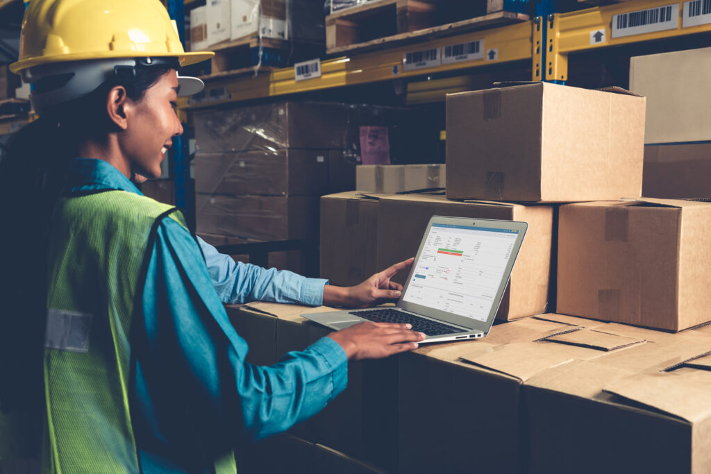 Woman in warehouse uses laptop with MachShip software