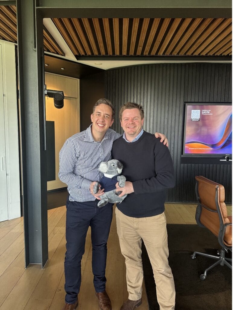 Brad Foot & Liam Mallett standing together in an office, smiling and holding a toy koala, symbolising the partnership between Fenwick Apps and MachShip.