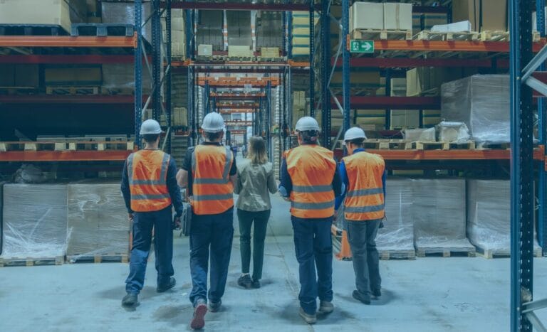 Five workers in safety vests walk through a warehouse, helping streamline freight operations.