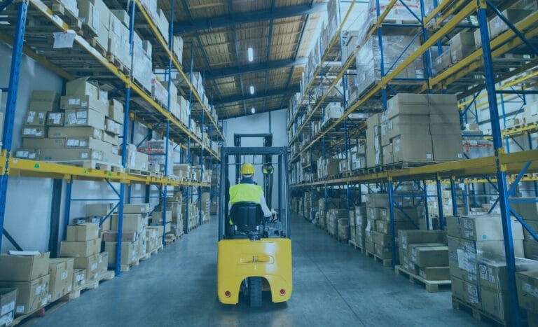 Worker drives a yellow forklift, boosting supply chain efficiency in a box-filled warehouse aisle.