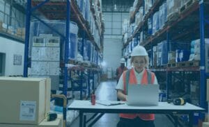 Woman in warehouse using spreadsheets on a laptop for modern freight cost management.