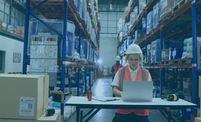 Woman in warehouse using spreadsheets on a laptop for modern freight cost management.
